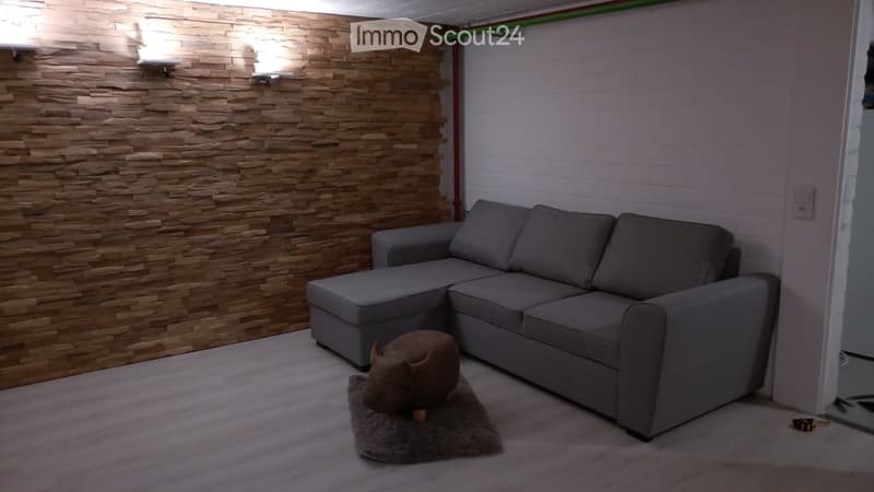 Modern living room with a grey sectional sofa, a small brown stool on a grey rug, and a textured wooden accent wall.