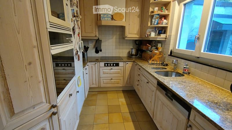 Bright kitchen with light wooden cabinets, granite countertop, stainless steel sink, and built-in oven. The space includes a refrigerator, dishwasher, and various kitchen utensils.
