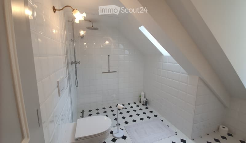 Modern bathroom with white tiles, black and white patterned floor, shower area with glass enclosure, toilet, and toilet paper holder.