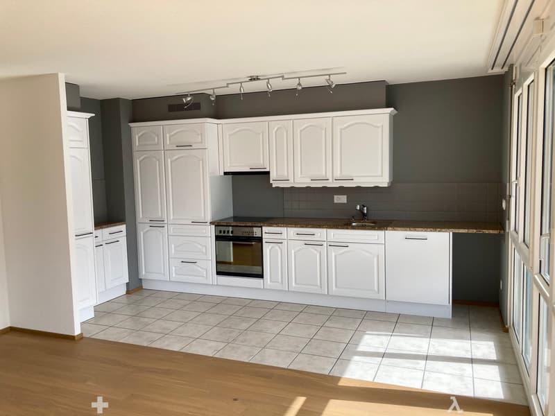 Modern kitchen with white cabinets, granite countertops, and a built-in oven. The space features tiled flooring and a wooden entryway.