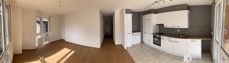 Bright, unfurnished living space with wooden flooring, white kitchen cabinets, an oven, and a sink.
