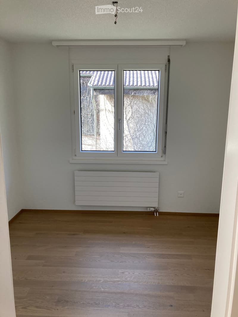 Empty room with wooden flooring, white walls, a window with frosted glass, and a radiator below it.