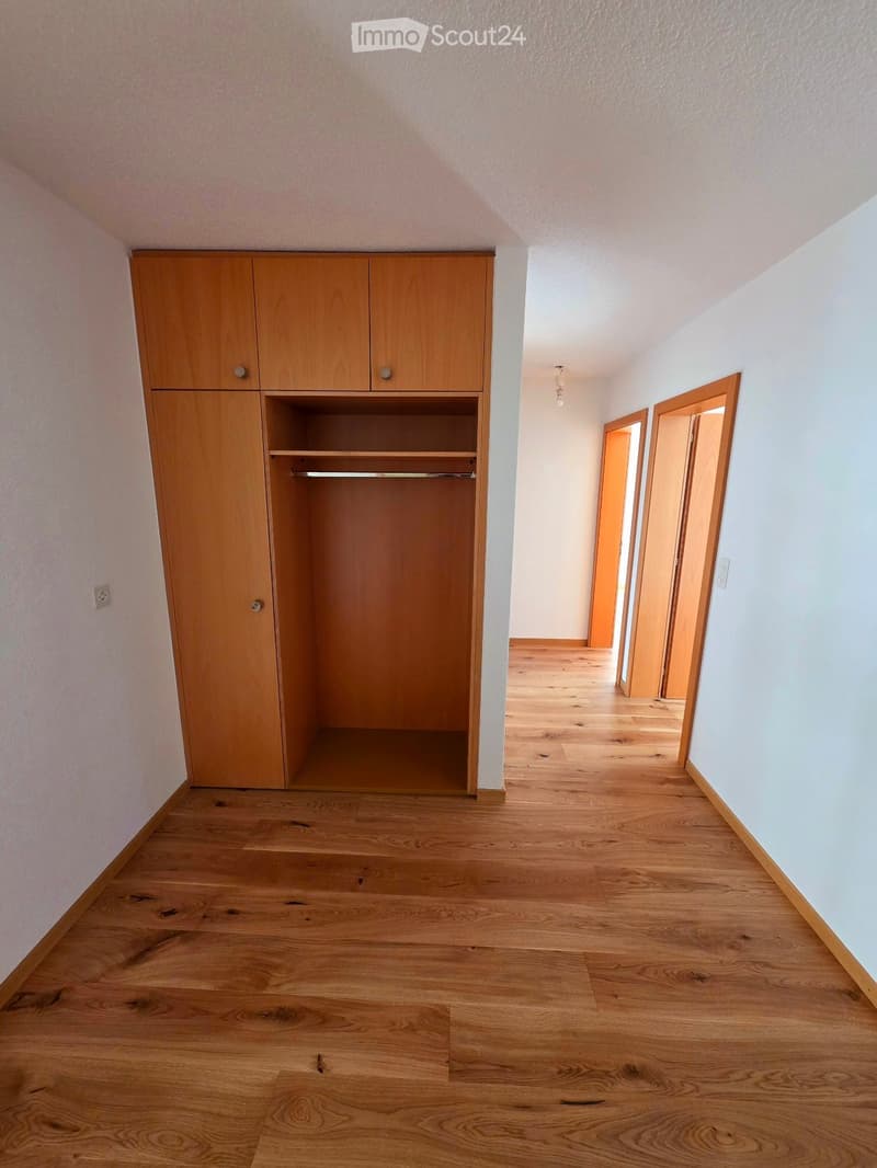 Empty hallway with wooden flooring, light-colored walls, and a built-in wooden closet with shelves and doors.