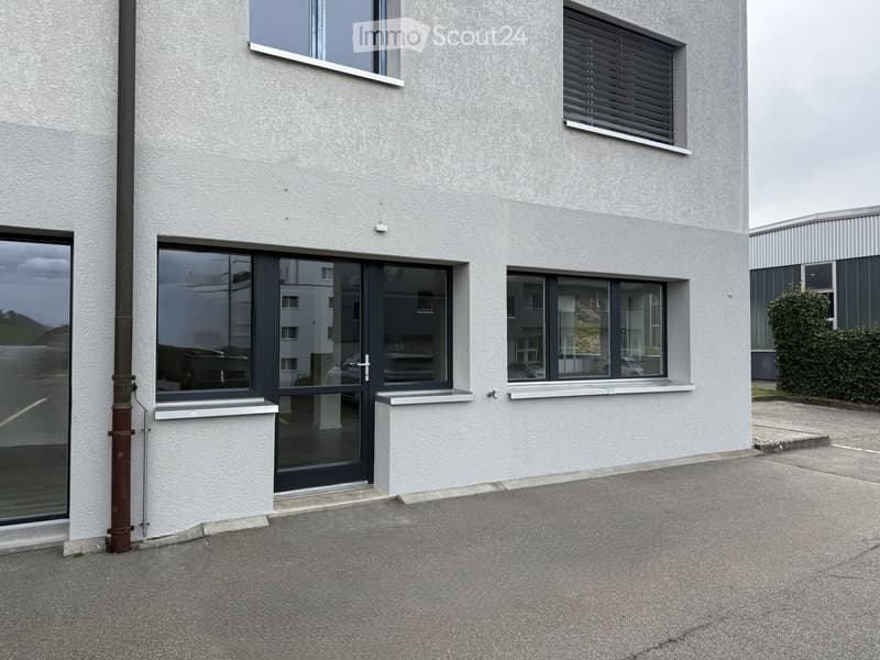 Modern two-story building with white textured walls, large windows, and a glass entrance door.