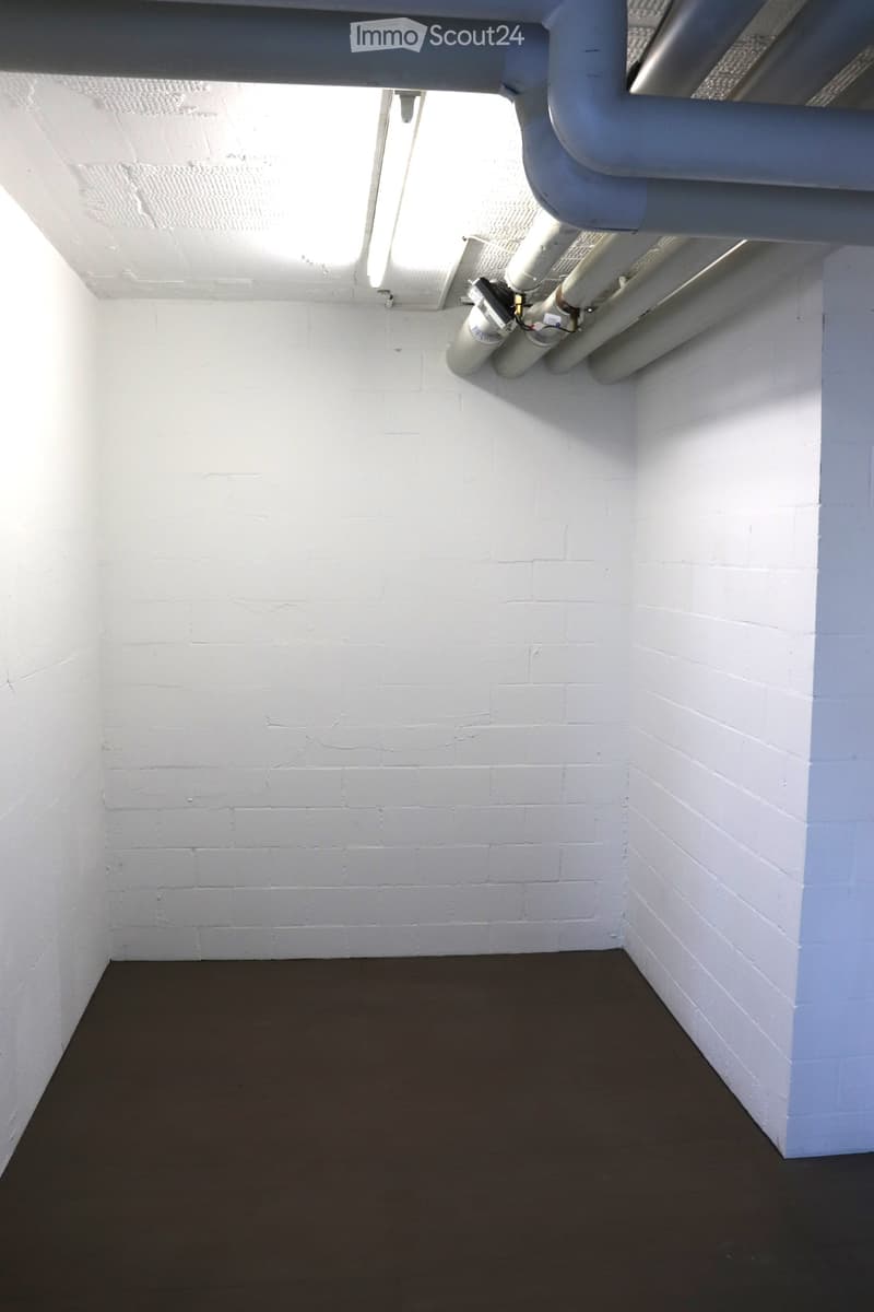 Empty room with white brick walls and a dark floor, featuring exposed pipes and a small window at the top.