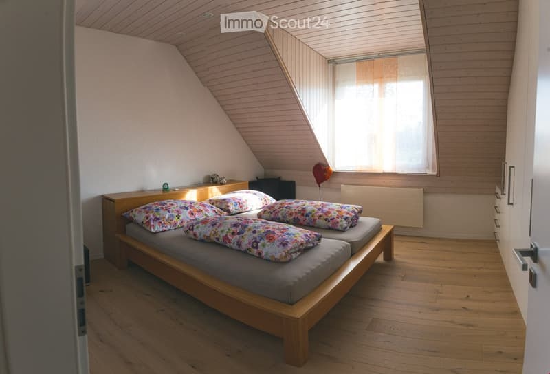 Cozy attic bedroom with wooden slanted ceilings, two single beds with colorful floral pillows, a small nightstand, and a balloon near the window.