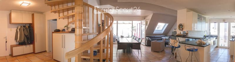 Open-plan living and dining area with a wooden spiral staircase leading to an upper level, modern kitchen with island, dining table with chairs, sofa, and bar stools.