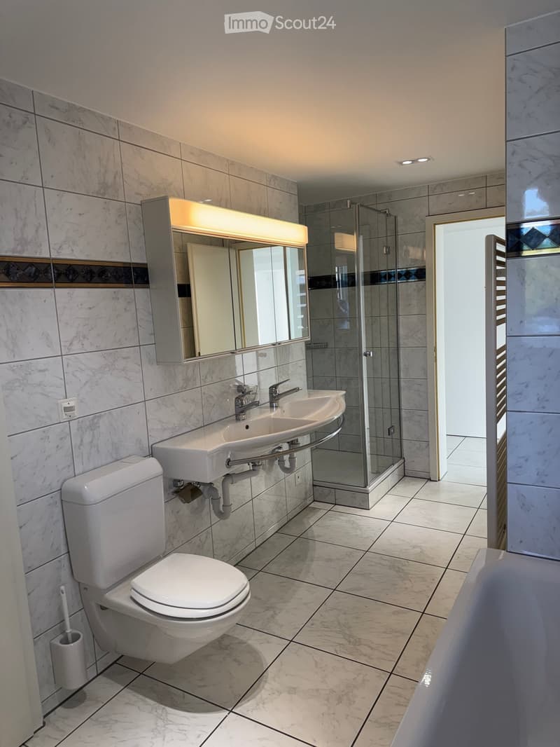 Modern bathroom with marble tiles, a toilet, a double sink, a bathtub, and a glass-enclosed shower area.