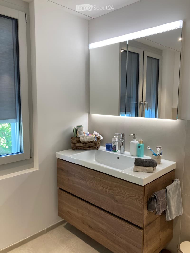 Modern bathroom with a double sink, wooden vanity, large mirror with LED lighting, and various toiletries.