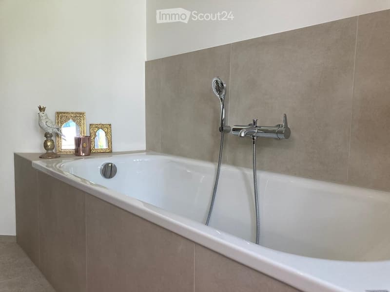 Modern bathroom with a large bathtub, chrome faucet, handheld showerhead, and decorative items on the edge of the tub.