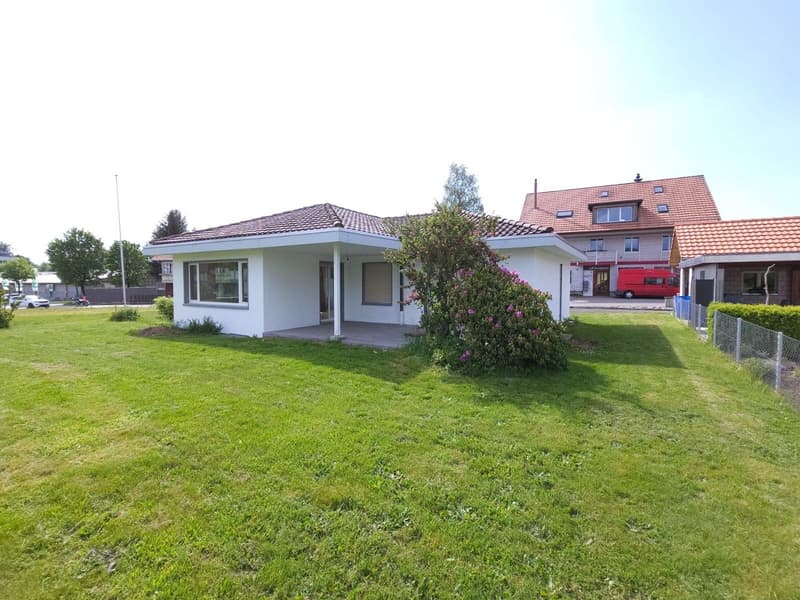 Single-story house with a red-tiled roof, white exterior, and a well-maintained lawn in front.