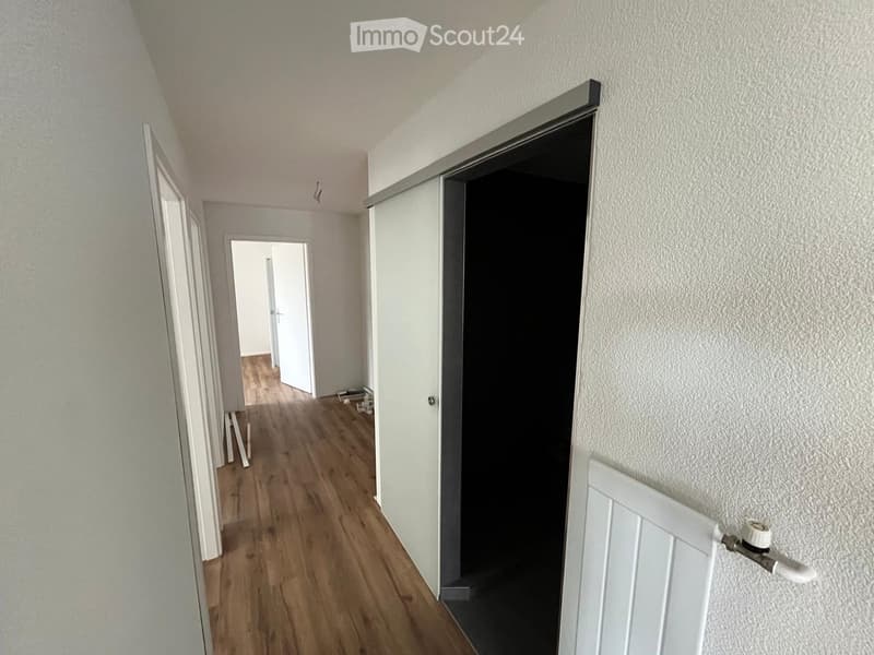 Empty hallway with wooden flooring, white walls, and multiple doors leading to other rooms.