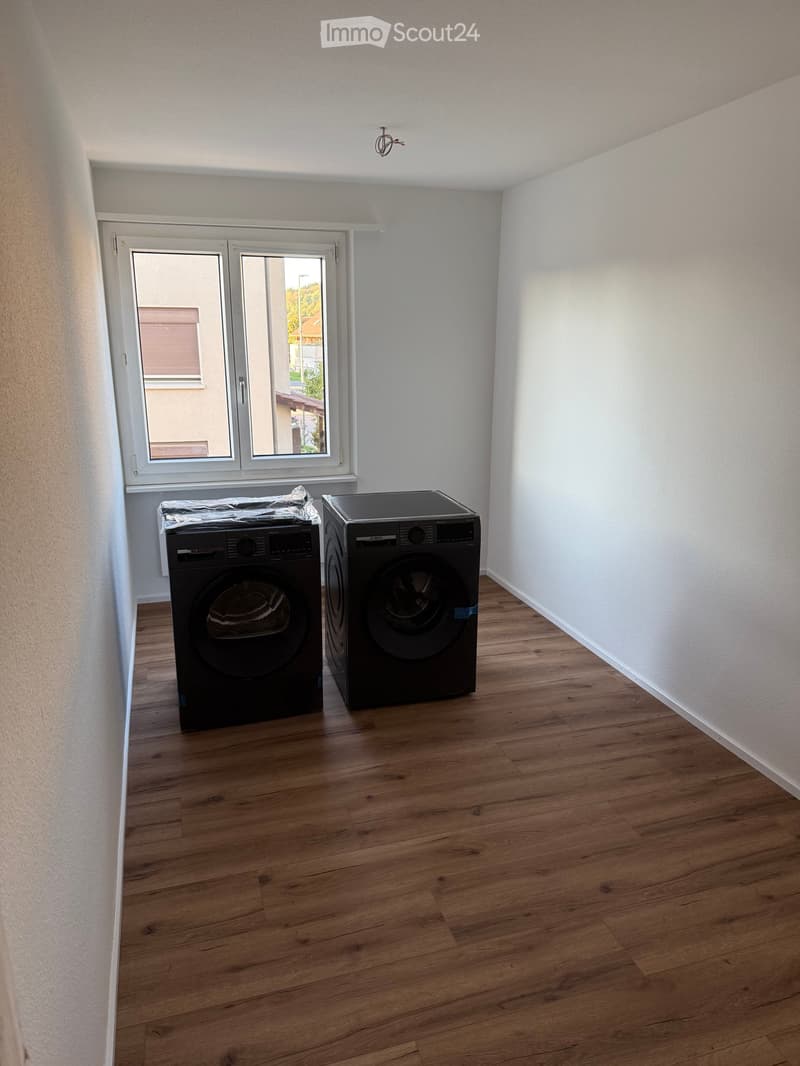 Bathroom with wooden flooring, white walls, and two black washing machines placed side by side near a large window.