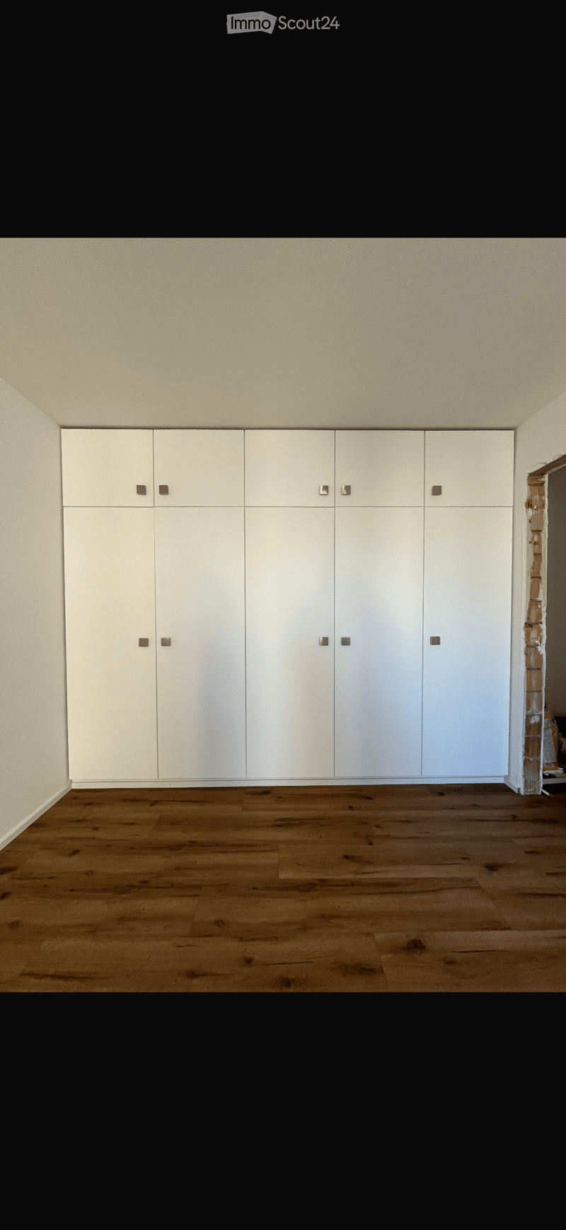 Empty room with light-colored walls, wooden flooring, and built-in white cabinets with silver handles.