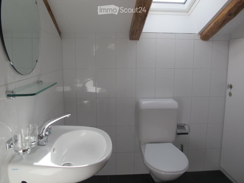 Modern bathroom with white tiles, a round sink, a toilet, a mirror, and a glass shelf holding a cup.