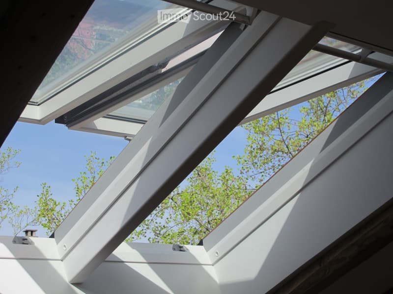 View of a modern white metal-framed skylight system with multiple panels, allowing natural light into the space. The sky and some greenery are visible through the open sections.