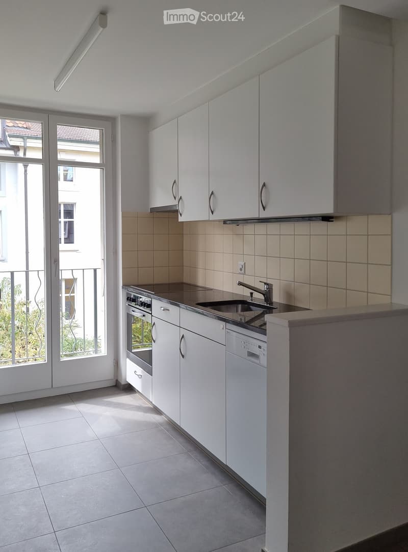 Modern kitchen with white cabinets, stainless steel appliances, and a view of the balcony.