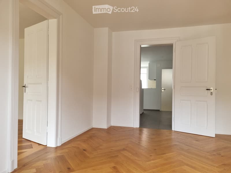 Empty hallway with wooden flooring, white walls, and two open doors leading to other rooms.