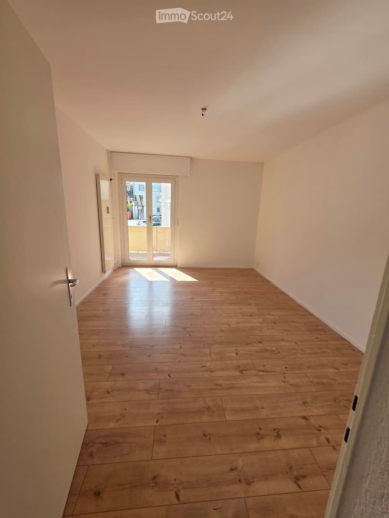 Empty room with wooden flooring, white walls, and a sliding glass door leading to an outdoor area.