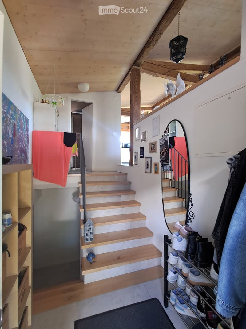 Wooden staircase with metal railing, shoe rack, and coat rack in a hallway with exposed wooden beams and white walls.