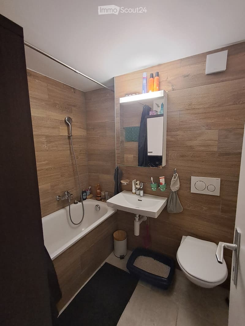 Modern bathroom with wooden walls, bathtub, sink, toilet, mirror, and various toiletries.