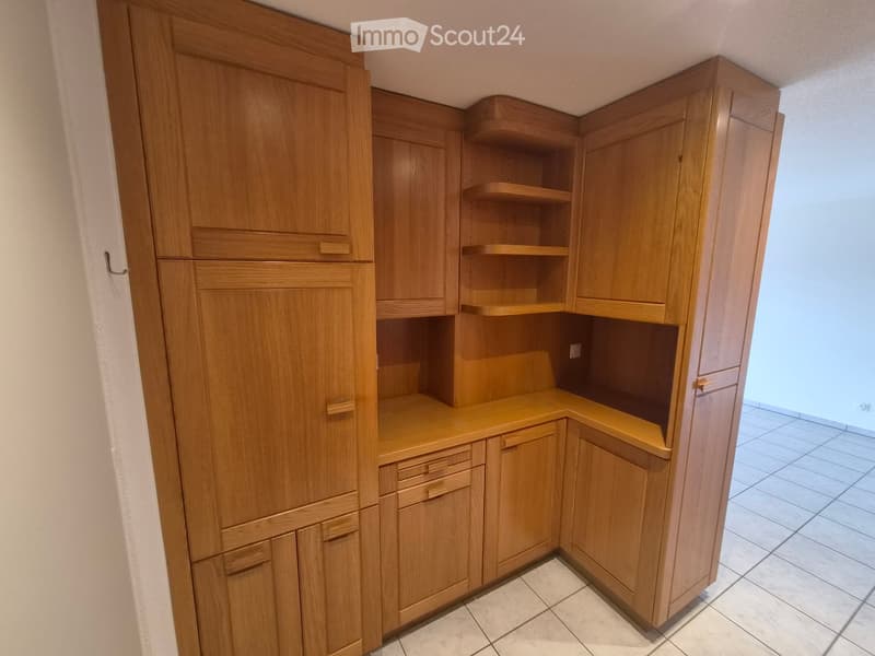 Corner kitchen area with light wooden cabinets, drawers, and open shelving units.