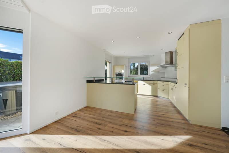Modern kitchen with light-colored cabinets, wooden flooring, and a central island with a glass railing. Features include an oven, range hood, and ample natural light from large windows.