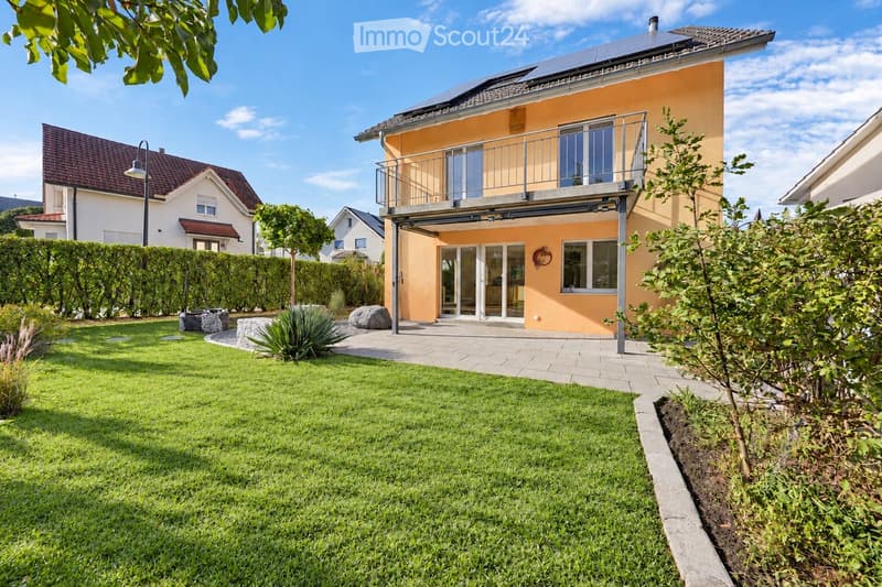 Well-maintained garden with green lawn, decorative rocks, and a modern house with a balcony and solar panels on the roof.