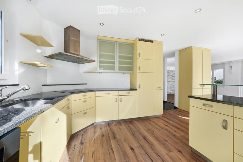 Modern kitchen with light yellow cabinets, granite countertops, stainless steel sink, and range hood. Wooden flooring and built-in storage.