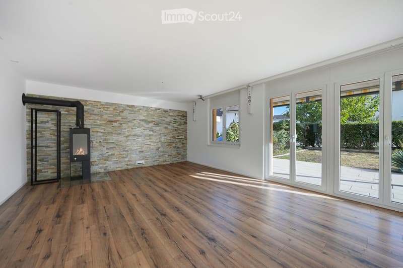 Bright, unfurnished living space with wooden flooring, large windows, and a modern fireplace.