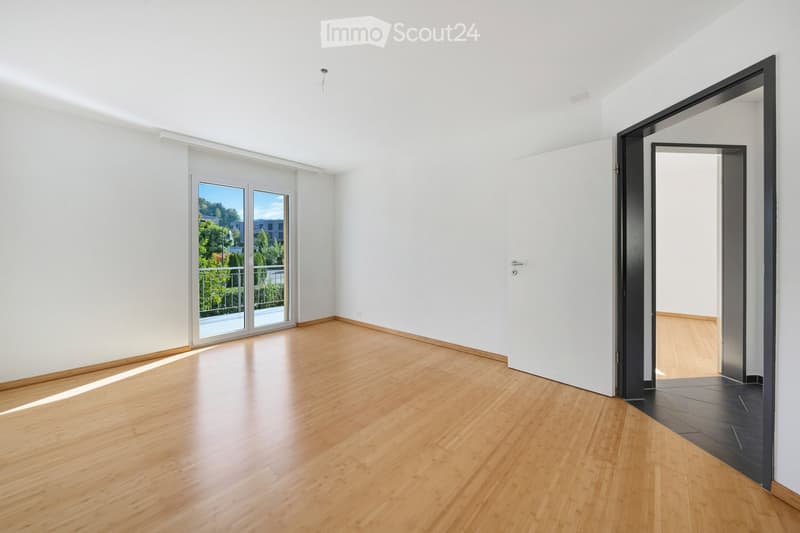 Empty room with light wooden flooring, white walls, and large sliding glass doors leading to a balcony.