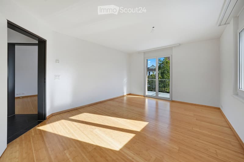 Empty room with light wooden flooring, white walls, and large sliding glass doors leading to a balcony.