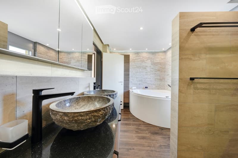 Modern bathroom with two stone sinks, black faucets, a white bathtub, and built-in cabinets.