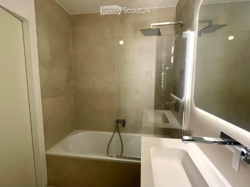 Modern bathroom with a bathtub, sink, mirror, and glass-enclosed shower area with multiple showerheads.