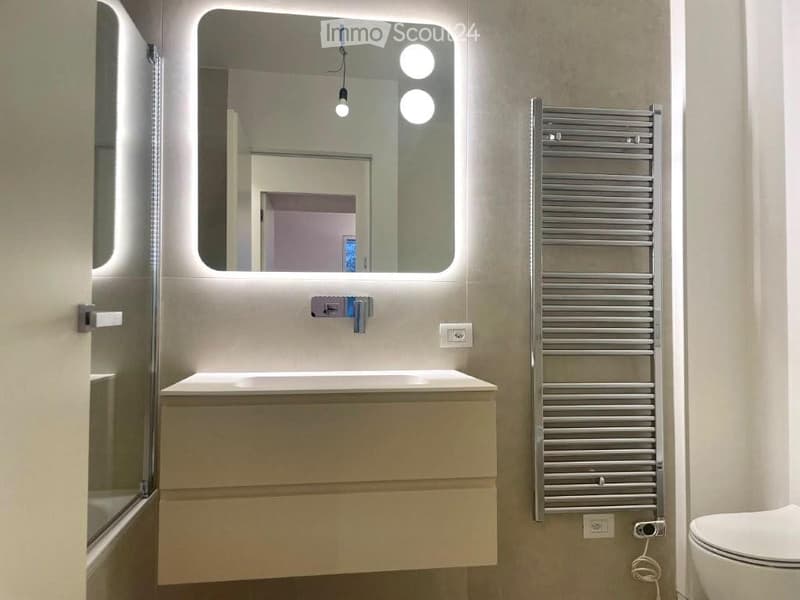 Modern bathroom with a white sink, illuminated mirror, chrome radiator, and toilet.
