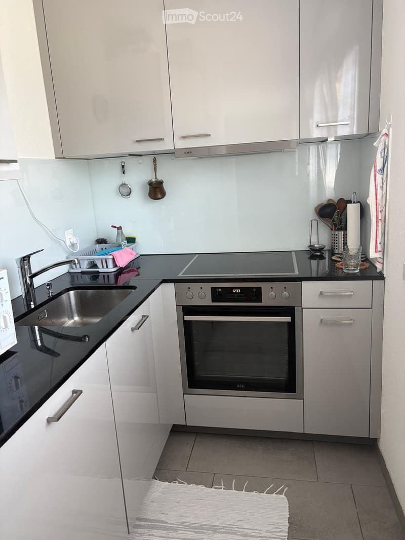 Modern kitchen with white cabinets, stainless steel appliances, and a black countertop. Features include an induction cooktop, oven, sink, and various kitchen utensils.