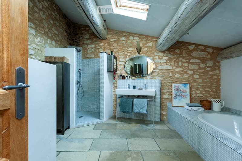 Bathroom with stone walls, a sink with a mirror above it, a bathtub, a shower, a towel rack with towels, and a cup on the sink counter.