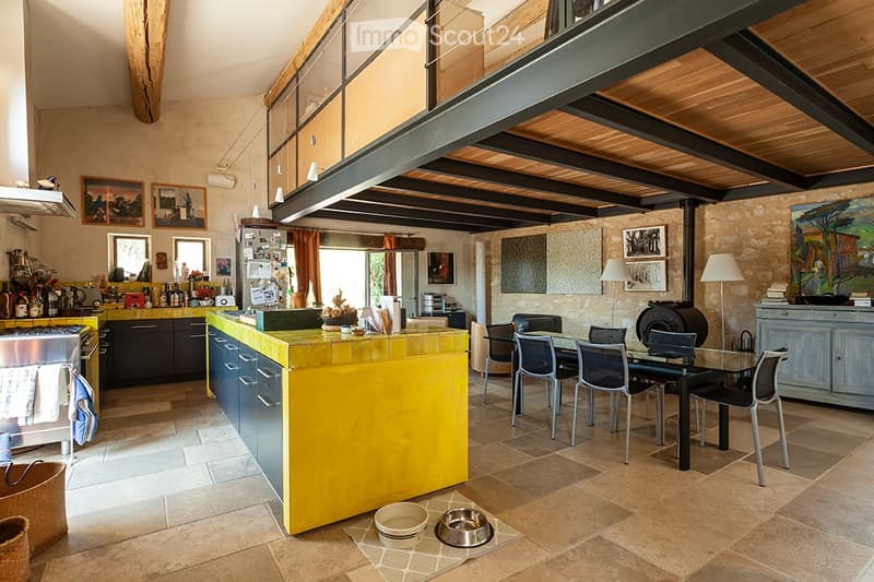 Open-plan kitchen and dining area with a yellow kitchen island, stainless steel appliances, dining table with chairs, and various kitchen items on counters.
