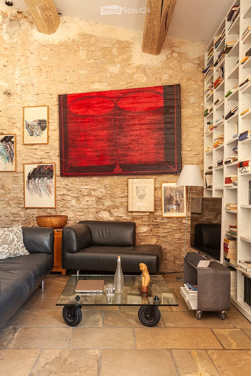 Living room with stone walls, leather sofa, glass coffee table, bookshelf, floor lamp, and artwork.