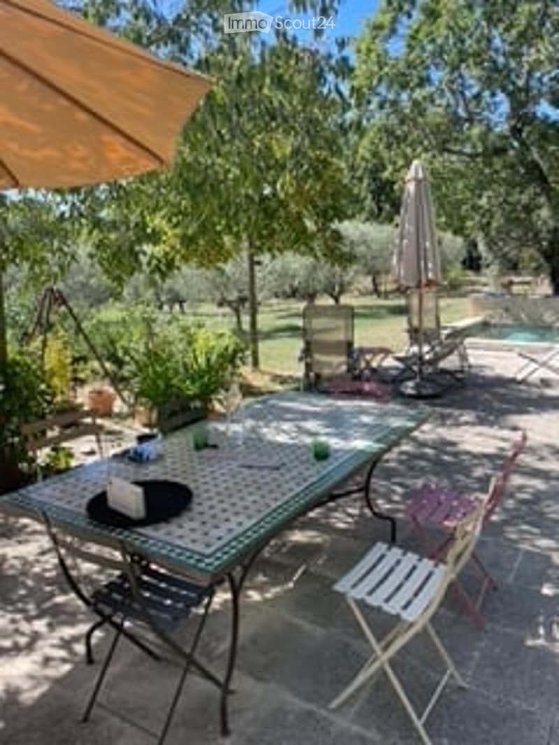 Outdoor patio area with a table, chairs, umbrella, and a swimming pool in the background.