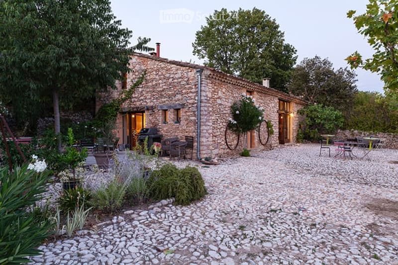 A rustic stone house with a gravel courtyard, outdoor seating, and greenery.