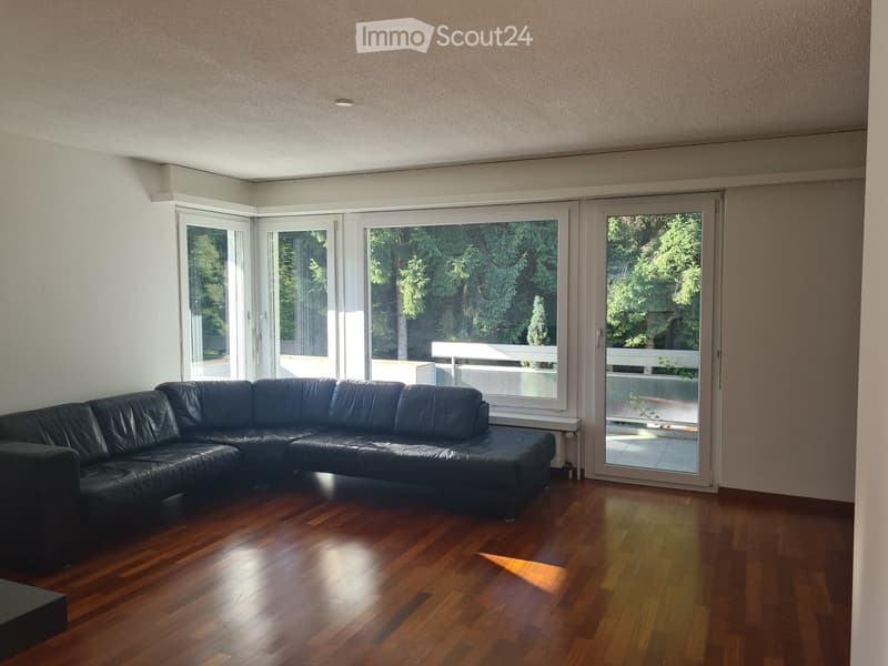 Modern living room with wooden flooring, large windows, and a black leather sectional sofa.