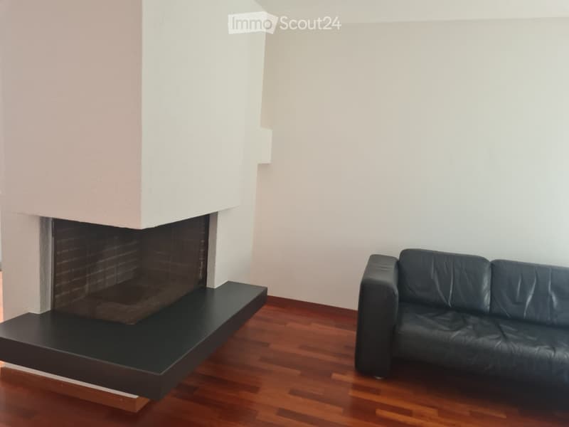 Modern living room with a dark leather sofa and a sleek black fireplace with a wooden floor.