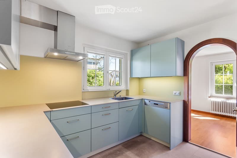 Modern kitchen with light blue cabinets, stainless steel sink, dishwasher, and a large window providing natural light.