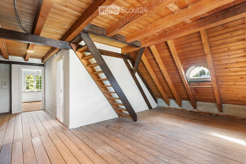 An empty attic space with wooden beams, exposed wooden ceiling, wooden floor, and a narrow wooden staircase leading upwards.