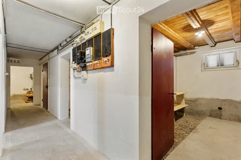Empty hallway with white walls, concrete floor, electrical panel, wooden door, and small window with blinds.