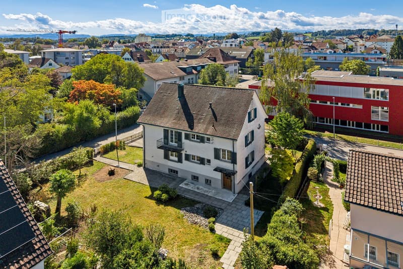 Aerial view of a residential house with a well-maintained garden, surrounded by other houses and greenery in a suburban neighborhood.