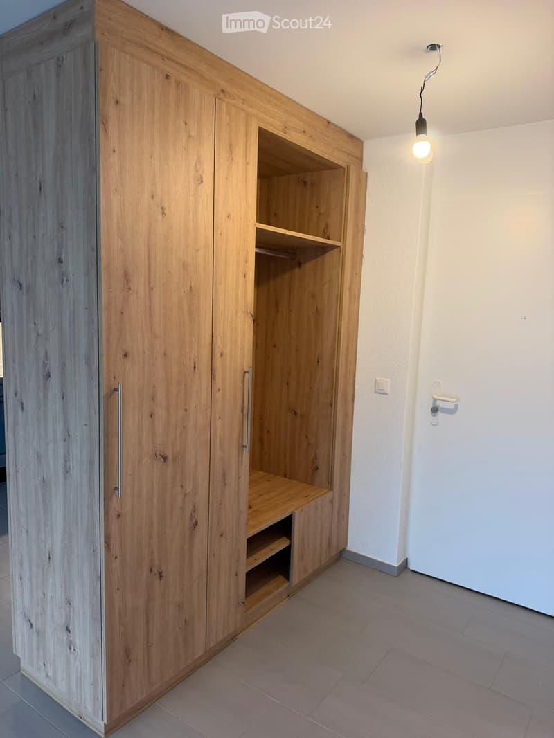 Empty room with light wooden built-in closet and shelves, white walls, tiled floor, and a hanging light fixture.