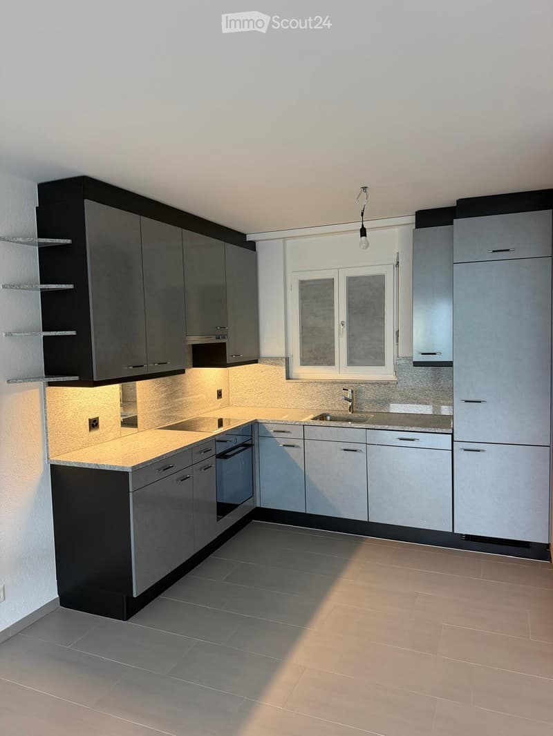 Modern kitchen with grey cabinets, a central island, and a window above the sink. Features include built-in appliances and sleek countertops.
