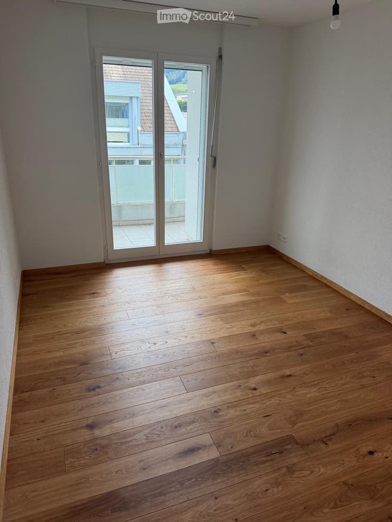 Empty room with wooden flooring, white walls, and a large sliding glass door leading to a balcony.